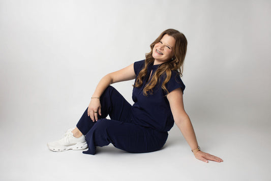 Kaila RDH, woman with long brown hair and braces, sitting on the floor an smiling.