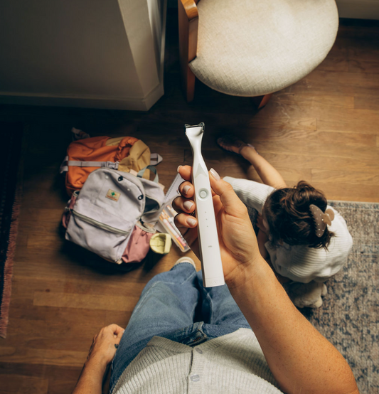 Woman standing holding a flosser about a pie of backpacks, with a girl sitting on the floor.