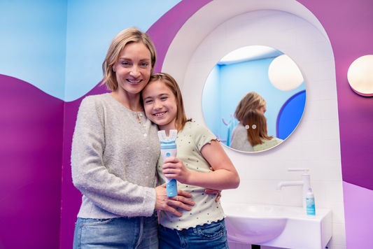 Mother and daughter standing in purple, multi-colored bathroom, holding Willo brushbot