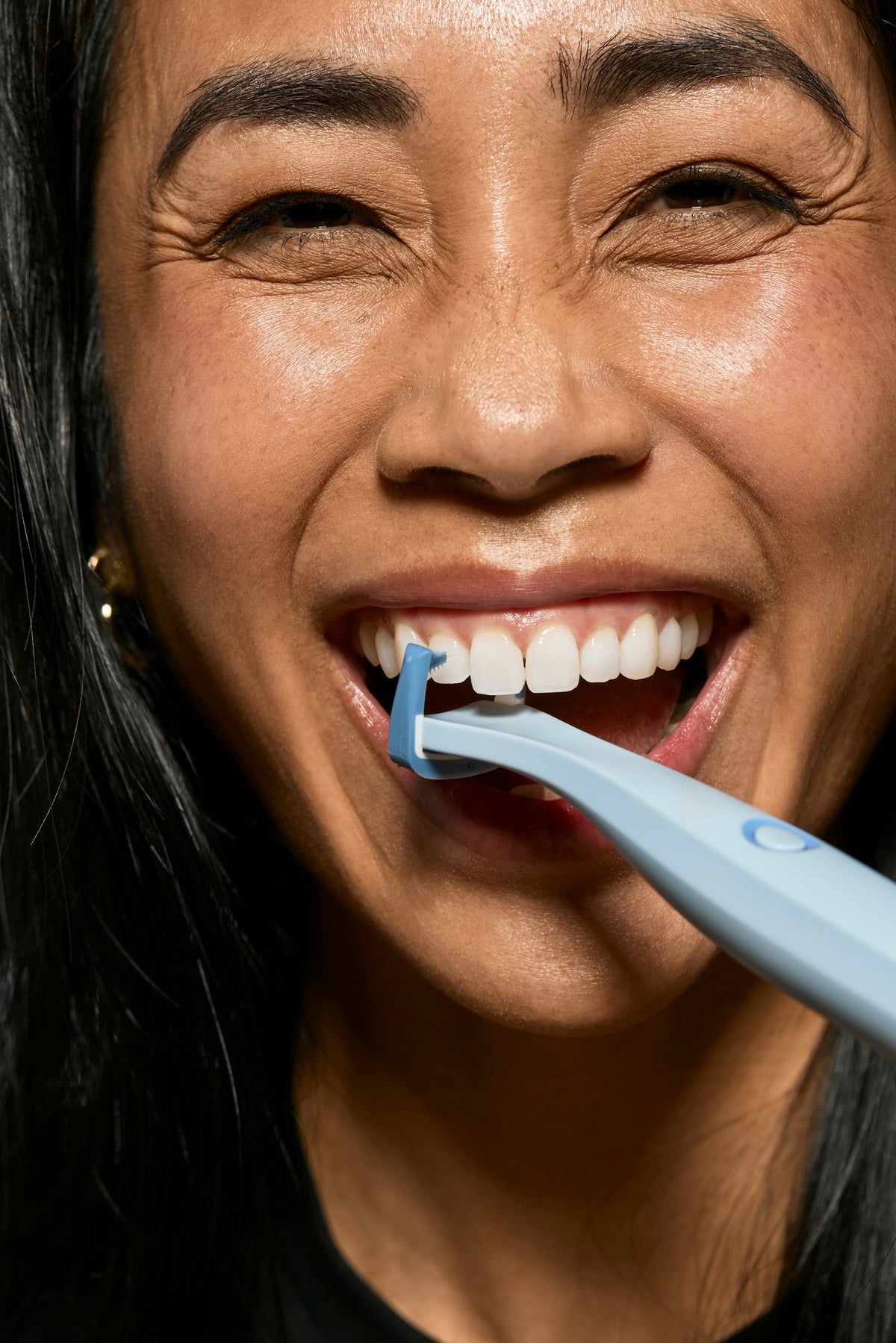 Woman smiling while using the blue Origin Flosser between her teeth