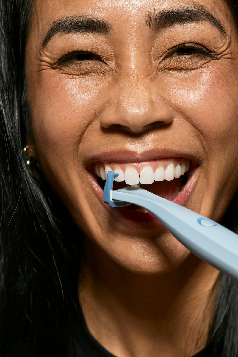 Woman smiling while using the blue Origin Flosser between her teeth